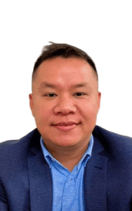 Person wearing a blue button-up shirt and a dark blazer against a white background.